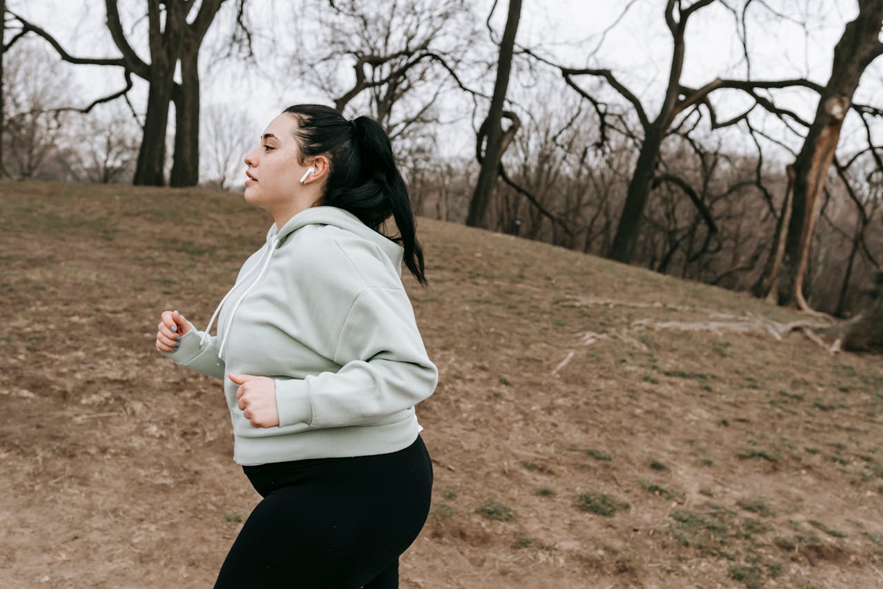 A young woman in activewear jogging through a park on a cool fall day.